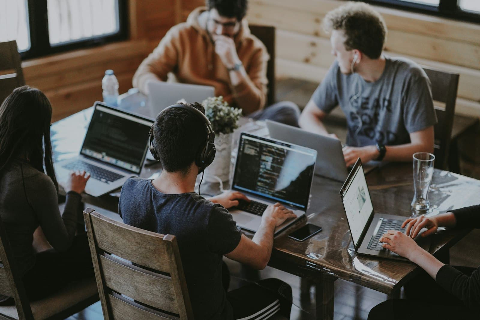 Engineering team around a shared table, multiple laptops with code on screen
